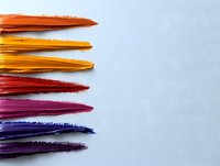 Vibrant paint brush strokes in warm and cool colors arranged horizontally on white background showcase artistic texture and gradient spectrum from orange to purple.