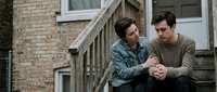 Young couple sitting on apartment building steps having intimate conversation in urban residential setting with brick architecture.