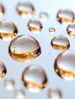 Golden water droplets scattered on white surface creating elegant reflective spheres with warm amber tones for luxury skincare and cosmetic applications.