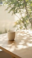 Empty ceramic mug on wooden table with dappled sunlight and blurred green foliage in background, suitable for beverage, lifestyle and product mockup designs.