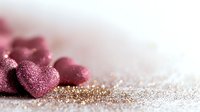Pink glittery heart decorations on shimmering golden background with soft focus and bokeh effect, romantic holiday celebration concept for valentines day.