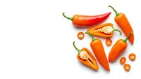 Fresh orange chili peppers scattered on white background with sliced pieces and seeds, isolated spicy vegetables for cooking and culinary design projects.