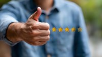 Male hand showing thumbs up gesture with five golden star rating floating above. Customer satisfaction and positive feedback concept on blurred background.