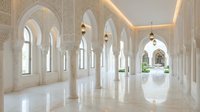 Elegant white marble corridor with ornate Islamic arches and columns creating stunning architectural perspective in luxury palace interior.