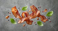 Crispy bacon strips with fresh basil leaves and peppercorns scattered on gray surface for culinary and cooking projects.