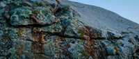 Weathered granite rock formation with colorful lichen growth and natural fractures against mountain backdrop in wilderness landscape setting.