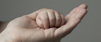 Tiny newborn fist resting gently in an adult open palm, symbolizing love, trust, family bond, and the miracle of new life.