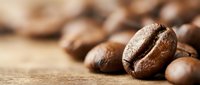 Close-up of roasted coffee beans on wooden surface with shallow depth of field, perfect for cafe branding and beverage marketing materials.