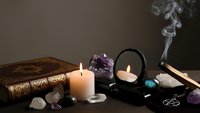 Mystical fortune telling setup with burning candles, crystals, mirror and ancient book creating atmospheric divination scene for spiritual practices.