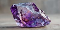 Raw amethyst crystal with deep purple hues and translucent layers showcasing natural geological formation on wooden surface.