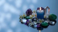 Spiritual healing crystals with burning candle and flowers arranged for meditation and wellness practices on reflective surface.