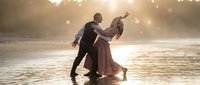 Romantic couple dancing on wet beach at golden sunset with warm bokeh lights creating dreamy atmosphere for wedding photography and love concepts.
