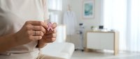 Woman holding a small pink ribbon in a medical office, symbolizing breast cancer awareness, hope, and support for health campaigns.