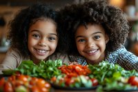 Young African American girls with natural curly hair smiling brightly at kitchen table with fresh colorful vegetables and healthy food spread, promoting healthy eating habits.