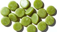 Fresh green round candies or mints scattered on white background with natural shadows, overhead view showing glossy sugar-coated surface texture.