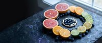 Fresh citrus fruits arranged in colorful circle with blueberries on dark slate surface near window. Healthy eating and vitamin C concept for nutrition content.