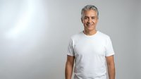 Confident mature Caucasian man in white t-shirt smiling at camera against neutral background for lifestyle and wellness marketing campaigns.