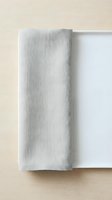 Rolled light gray linen napkin or kitchen towel placed next to white ceramic plate on natural wood surface for dining and tableware design use.