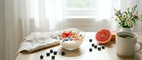 Healthy breakfast bowl with granola, yogurt, fresh blueberries and strawberries on wooden table with grapefruit, tea and flowers.