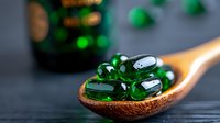 Green translucent soft gel capsules on wooden spoon against dark background, medicine and pharmaceutical concept for health supplements and vitamins.