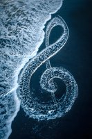 Aerial view of ocean waves forming treble clef music note shape on dark sandy beach, creating natural harmony between sea and shore.