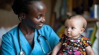 African American female pediatrician in blue scrubs and stethoscope examining happy baby patient during medical checkup, showing caring and professional approach in healthcare setting.