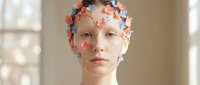 Young woman with colorful paper flowers adorning her head and face in artistic portrait for creative projects and beauty concepts.