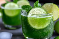 Refreshing green cocktail with lime slice and mint garnish, served in clear glass with ice cubes for summer entertaining.