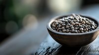 Fresh whole white peppercorns in rustic wooden bowl on dark table with soft bokeh background, macro food photography for culinary and spice concepts.