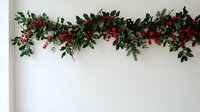 Festive red flower and green leaf garland draped along white wall for holiday decoration, wedding backdrop, event styling, and seasonal home decor.