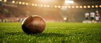 American football on green grass field with stadium lights and blurred crowd background for sports and recreation concepts.