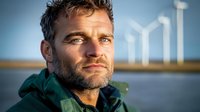 Professional Caucasian male engineer with beard at offshore wind farm facility during golden hour sunset for renewable energy industry projects.