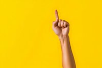 Female hand with raised index finger against vibrant yellow background, suggesting attention, idea moment or number one gesture. Positive communication concept.