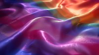 Vibrant waves of colorful satin fabric with smooth folds creating abstract flowing pattern in purple, pink, orange and blue tones. Luxurious textile background.