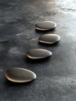 Four smooth polished stones arranged in diagonal line on dark textured surface with soft lighting for spa wellness meditation and mindfulness concepts.