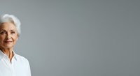 Senior woman with white hair wearing white shirt smiling at camera against neutral gray background. Portrait suitable for healthcare, business, corporate and lifestyle content.