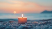 Glowing candle on pebble beach at sunset with ocean waves and mountain silhouette in background, creating serene coastal atmosphere.