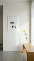 Minimalist interior with be kind framed poster on white wall, wooden bench, and yellow tulip in glass vase, sunlight casting soft shadows.