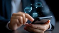 Business person using smartphone with glowing chat message icons floating above, representing digital communication and mobile messaging technology.
