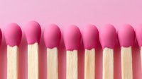 Pink matches lined up in row on pink background, minimalist composition showing wooden sticks with round pink tips creating repetitive pattern.
