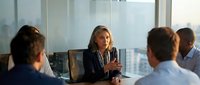 Professional businesswoman leading corporate meeting in modern conference room with city skyline view during daytime discussion.