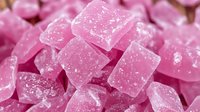 Pink sugar-coated candy cubes in macro shot showing crystalline texture and sparkly surface, sweet treats background pattern for confectionery and dessert designs.