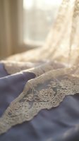 Delicate ivory lace trim draped over soft blue fabric near a sunlit window, creating elegant shadows and warm natural lighting for wedding, bridal, or textile design projects.