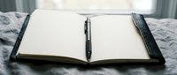 Open blank notebook with black pen on bed ready for writing thoughts ideas planning journaling creative work business notes personal diary entries.