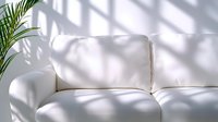 White modern couch with palm leaf shadow and sunlight through window creating geometric patterns on clean minimalist furniture, bright interior design.