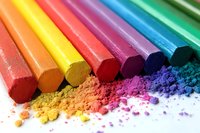 Colorful chalk pastels arranged in rainbow order with vibrant powder pigments scattered below, showing texture and artistic medium on white background.