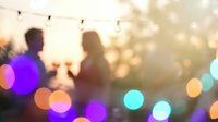Blurred silhouettes of people at evening party with colorful bokeh lights and string lighting creating warm festive atmosphere for celebrations.