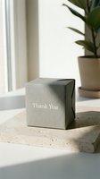 Gray kraft paper gift box with Thank You text on marble surface, soft natural light, green plant background, minimal elegant packaging concept.