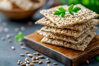 Crispy whole grain crackers with seeds stacked on wooden board, garnished with fresh parsley leaves and scattered sunflower seeds, healthy snack concept.