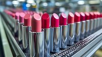 Rows of pink and red lipsticks in metallic tubes on cosmetic factory production line, selective focus on shiny chrome packaging and vibrant makeup colors.